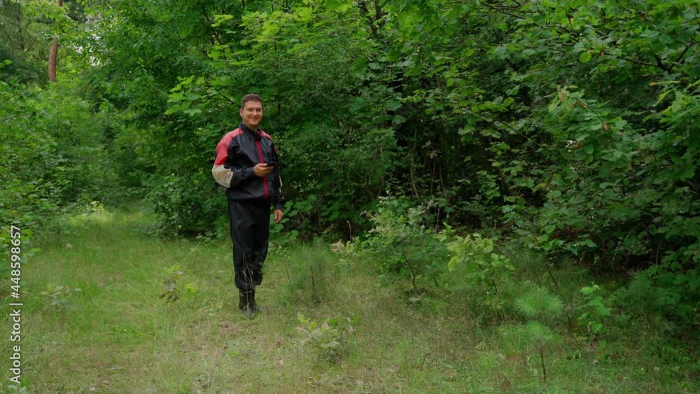 Man holding typing smartphone looking at camera in forest. Attractive 30s young adult male person using modern telephone gadget and online internet technology. Happy buyer customer standing outdoors Man holding typing smartphone looking at camera in forest. Attractive 30s young adult male person using modern telephone gadget and online internet technology. Happy buyer customer standing outdoors