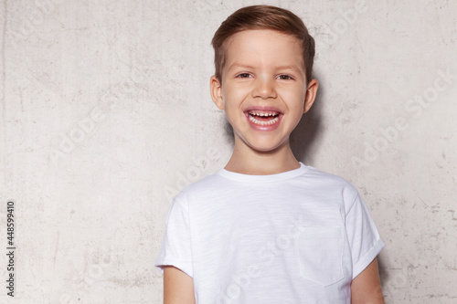 Cheerful caucasian child boy laughing feels overjoyed having wide toothy smile, posing on gray studio background. Happy little schoolboy having fun expressing sincere positive emotions.