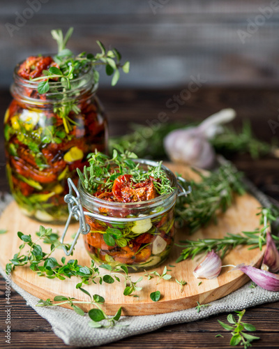 Dried tomatoes with herbs and spices. Seasonal appetizer of vegetables. Rosemary, garlic, thyme on a wooden background. Fresh harvest. A can of baked tomatoes. Italian food. Italian cuisine