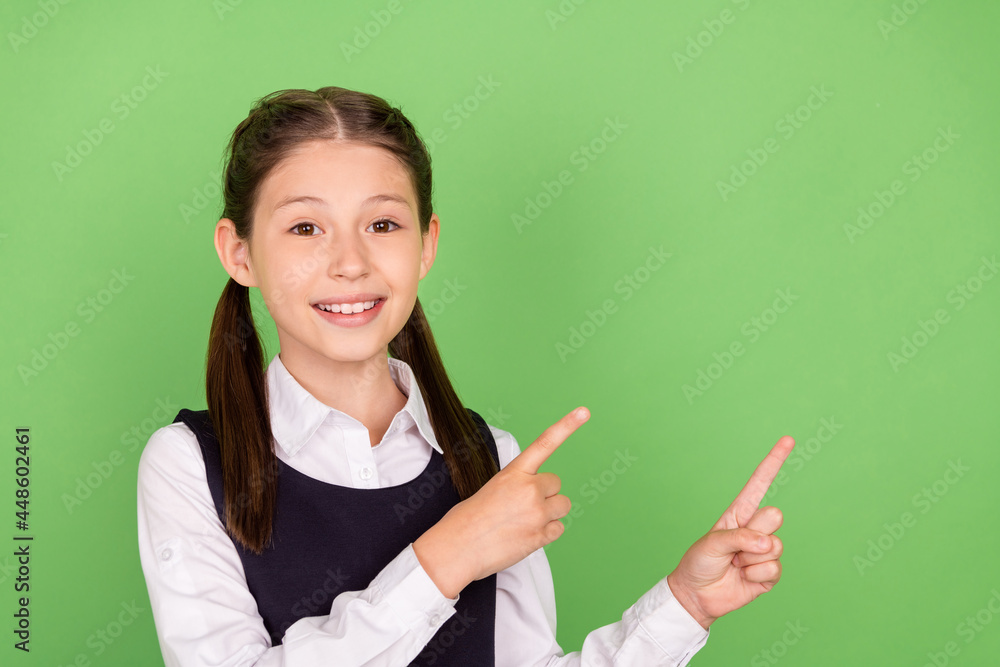Photo of young school girl happy positive smile indicate fingers empty space ad advise promo isolated over green color background Photo of young school girl happy positive smile indicate fingers empty space ad advise promo isolated over green color background