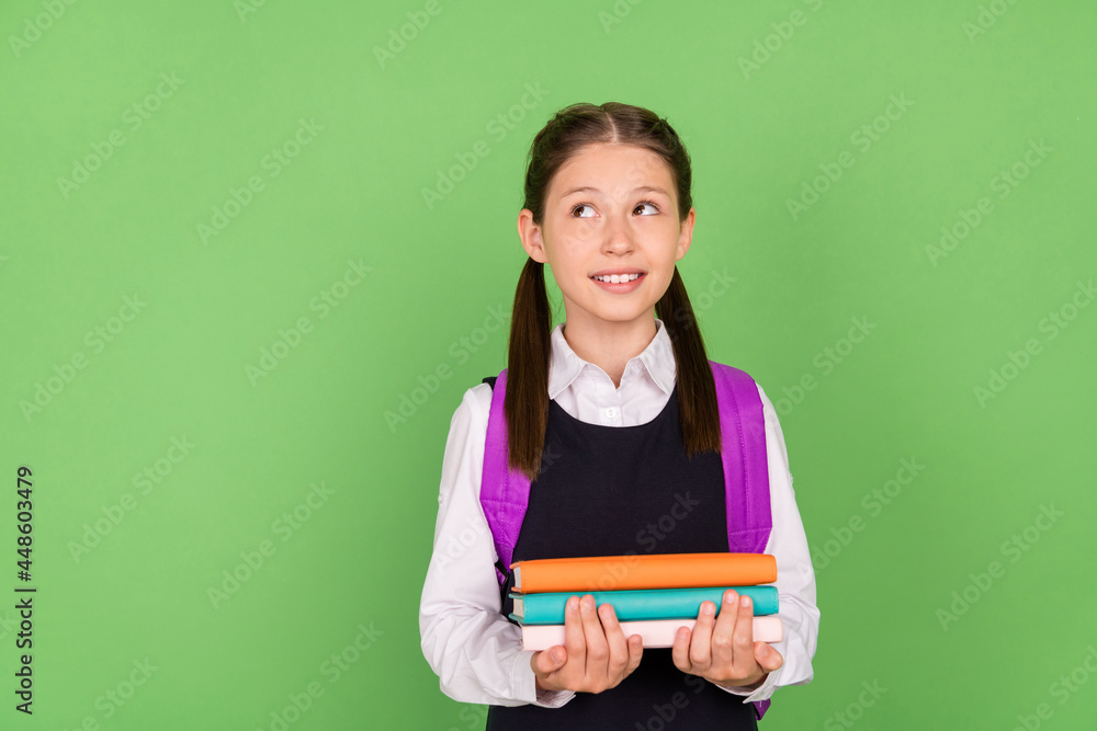 Photo portrait schoolgirl with backpack showing looking empty space dreamy with book pile isolated pastel green color background Photo portrait schoolgirl with backpack showing looking empty space dreamy with book pile isolated pastel green color background