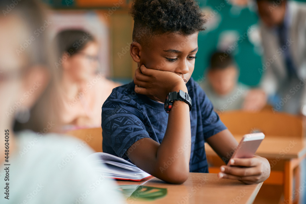 Black elementary student typing text message on smart phone in classroom. Black elementary student typing text message on smart phone in classroom.
