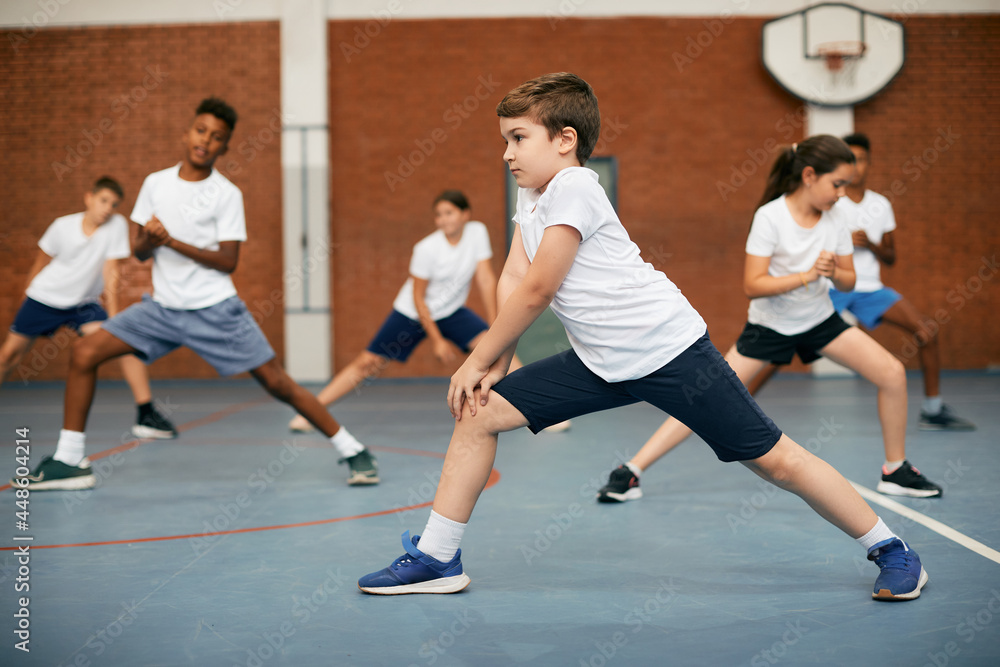 Elementary student and his friends warming up during PE class at school gym.