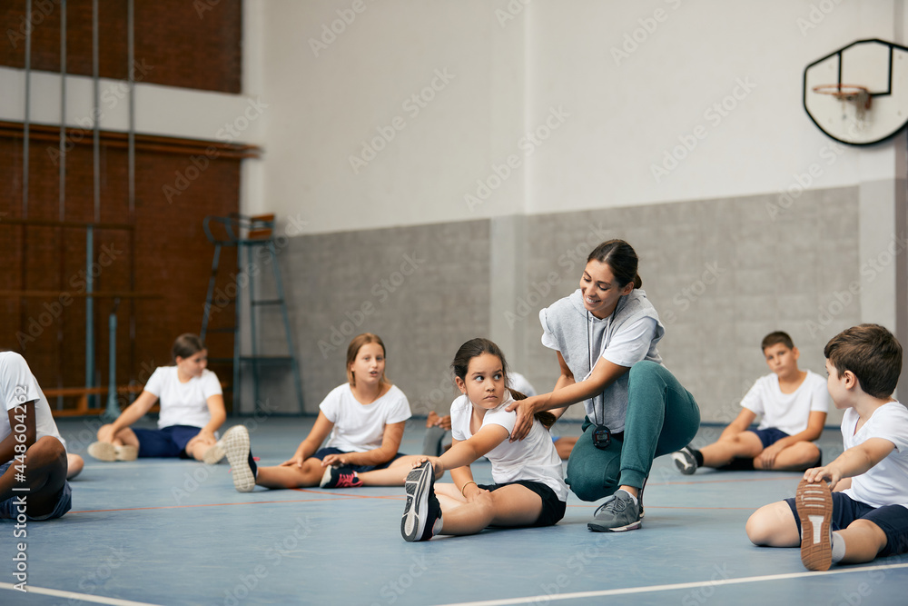 Happy female PE teacher having class with group of elementary students at school gym. Happy female PE teacher having class with group of elementary students at school gym.