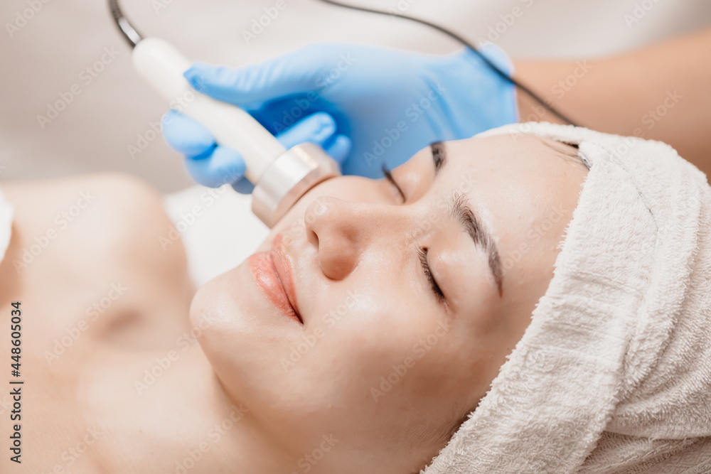 Ultrasonic facial skin massage with women happy face skincare tightening in beauty salon spa.
