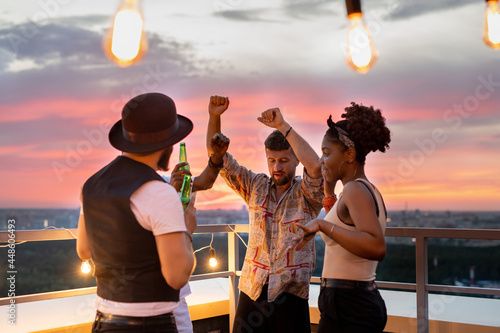 Group of young people dancing and having beer at party on rooftop patio photo