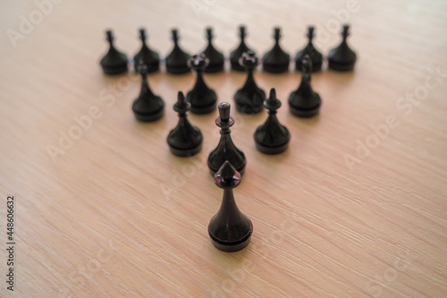 black chess pieces arranged in the shape of a pyramid on a wooden surface
