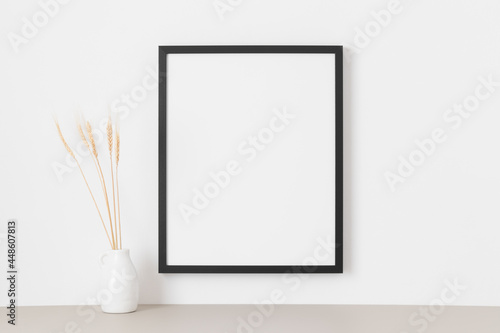 Black frame mockup on the wall with a dried flower decoration.
