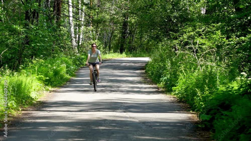 A girl in sunglasses rides a bicycle along a forest road. The girl pedals the bike with a smile. A girl in sunglasses rides a bicycle along a forest road. The girl pedals the bike with a smile.