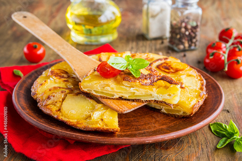 Spanish tortilla, traditional dish with eggs and fried potatoes on a clay plate on a wooden background. Potato recipes.