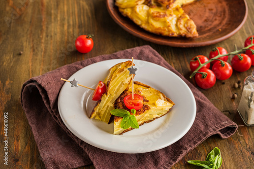 Sliced Spanish tortilla, a traditional dish with eggs and fried potatoes on a clay plate on a wooden background. Potato recipes.