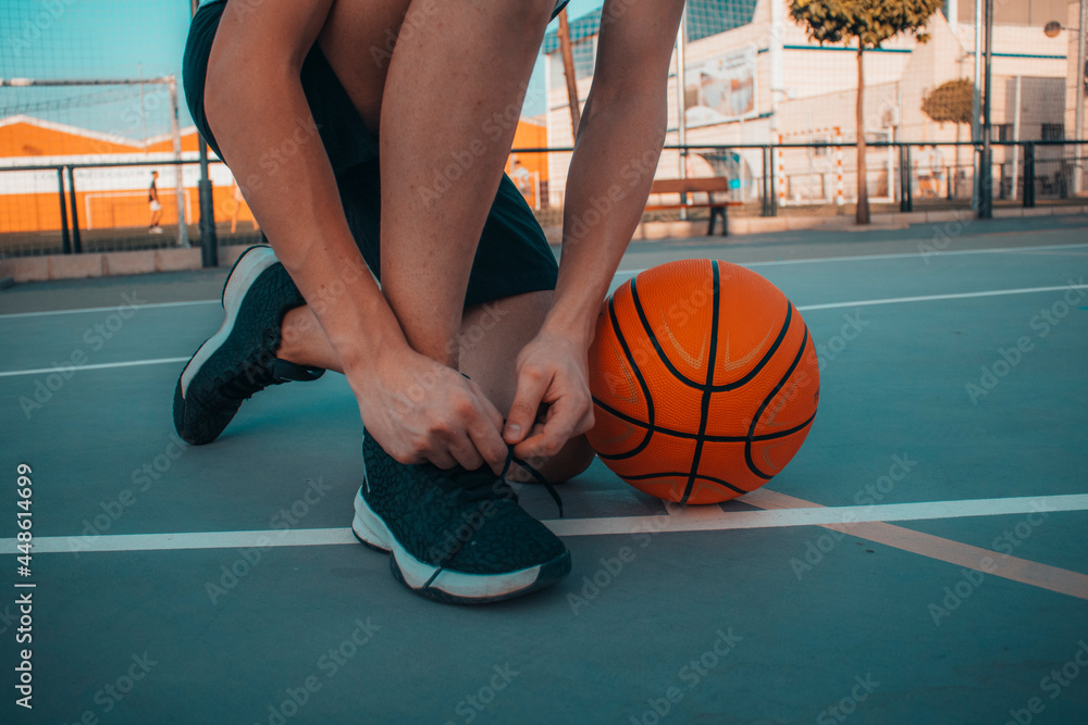 Jugador de baloncesto junto con el balon en la pista atandose los cordones  para prepararse en el partido foto de Stock | Adobe Stock
