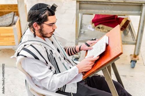 Orthodox Jewish man, wearing phylacteries (tefilin) and shawl (tallit), sitting praying at the Western Wall, Jerusalem. photo