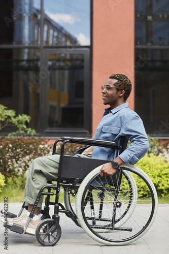 Side view of smiling African-American disabled man in glasses sitting in wheelchair while spending time outdoors © Seventyfour