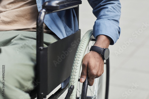 Close-up of unrecognizable black invalid in wristwatch spinning wheel of wheelchair outdoors