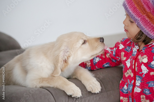Fototapeta Naklejka Na Ścianę i Meble -  Linda criança com roupa branca e óculos de sol brincando com cachorro Golden Retriever .

