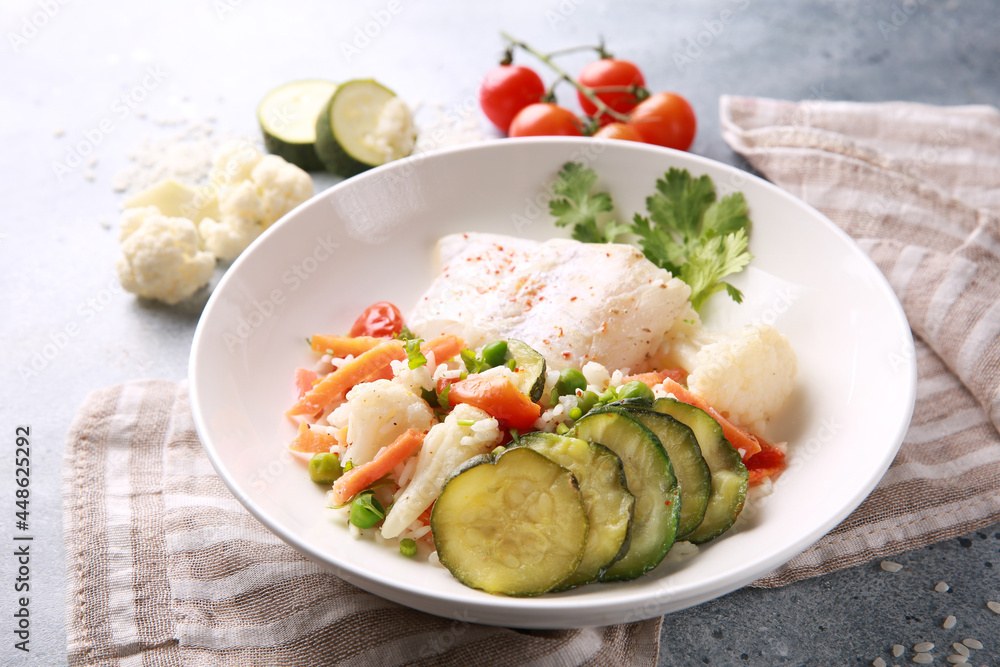 Seafood dish. White fish with rice and vegetables: zucchini, cauliflower, carrots, tomatoes and herbs in a white plate on a gray background. Background image, copy space Seafood dish. White fish with rice and vegetables: zucchini, cauliflower, carrots, tomatoes and herbs in a white plate on a gray background. Background image, copy space