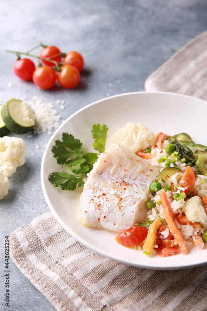 Seafood dish. White fish with rice and vegetables: zucchini, cauliflower, carrots, tomatoes and herbs in a white plate on a gray background. Background image, copy space Seafood dish. White fish with rice and vegetables: zucchini, cauliflower, carrots, tomatoes and herbs in a white plate on a gray background. Background image, copy space