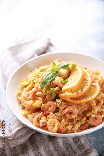 Healthy food. A seafood dish. Risotto with shrimp, scallops, lemon and fresh herbs in a white plate on a bright table. Background image, copy space