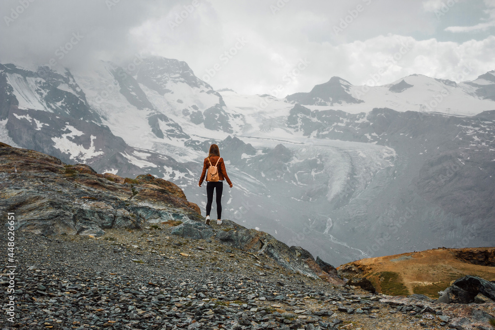 Girl, woman with backpack in the leather jacket on the mountain background. Top of the Gornergrat near Matterhorn, Zermatt, Switzerland. Swiss Alps hiking. Adventure in Europe. Tourist. Girl, woman with backpack in the leather jacket on the mountain background. Top of the Gornergrat near Matterhorn, Zermatt, Switzerland. Swiss Alps hiking. Adventure in Europe. Tourist.