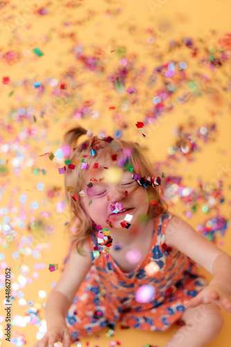 Toddler girl playing with colorful confetti in front of yellow backdrop 