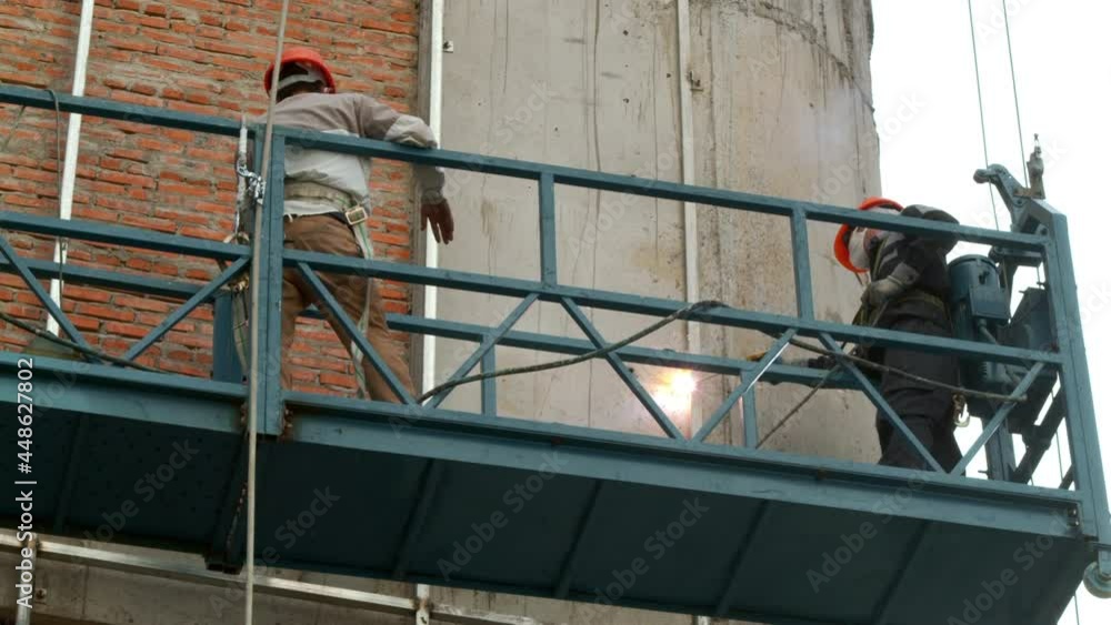 Industrial workers welding metal structures, male welders brazing a steel beam on a new building at a construction site. the welder is working. Sparks fly like a welder welds steel. builder Industrial workers welding metal structures, male welders brazing a steel beam on a new building at a construction site. the welder is working. Sparks fly like a welder welds steel. builder
