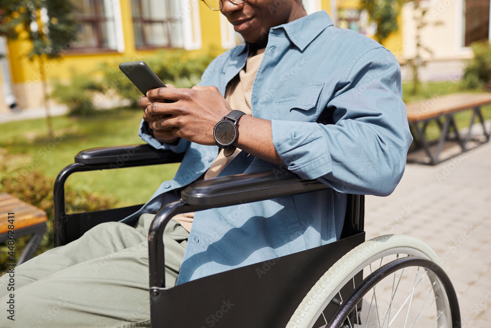 Close-up of content disabled man in blue shirt sitting in wheelchair and using smartphone while reading news on internet outdoors Close-up of content disabled man in blue shirt sitting in wheelchair and using smartphone while reading news on internet outdoors
