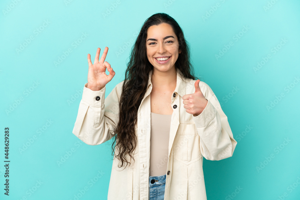 Young caucasian woman isolated on blue background showing ok sign and thumb up gesture Young caucasian woman isolated on blue background showing ok sign and thumb up gesture