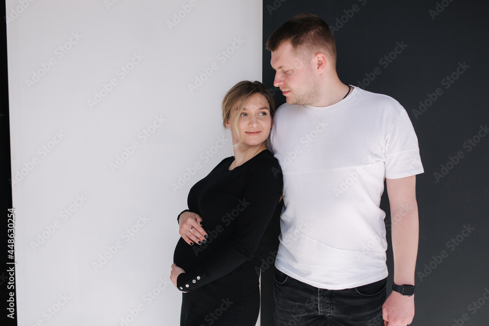 Pregnant woman with her lovely husband hug each other and put hand on belly. Studio photosession. Black and white background Pregnant woman with her lovely husband hug each other and put hand on belly. Studio photosession. Black and white background