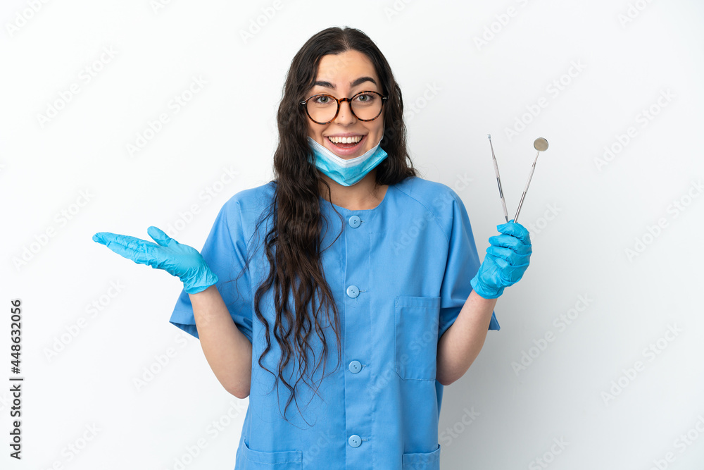 Young woman dentist holding tools isolated on white background with shocked facial expression
