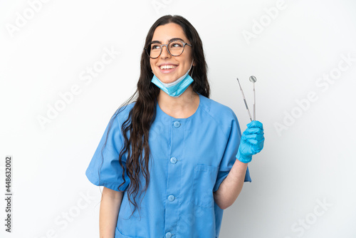 Young woman dentist holding tools isolated on white background thinking an idea while looking up