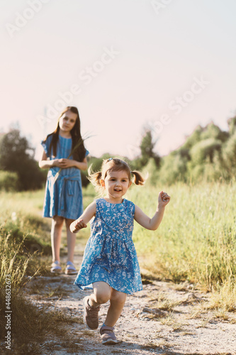 Little girl running in summer grass field with scene path. Two sisters walking together and enjoy calm sunny day