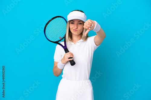 Young tennis player Romanian woman isolated on blue background showing thumb down with negative expression © luismolinero