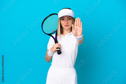 Young tennis player Romanian woman isolated on blue background making stop gesture © luismolinero