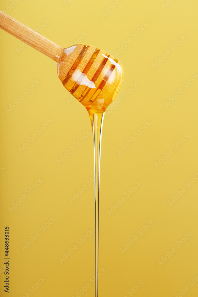 Honey drips in a thin stream from a honey dipper on a yellow background. Honey drips in a thin stream from a honey dipper on a yellow background.