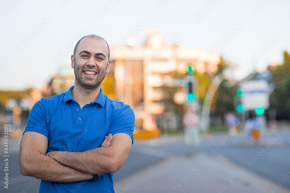 Cheerful and smiling young man with arms crossed posing on a street with traffic lights in the background. includes copy and text space. Cheerful and smiling young man with arms crossed posing on a street with traffic lights in the background. includes copy and text space.