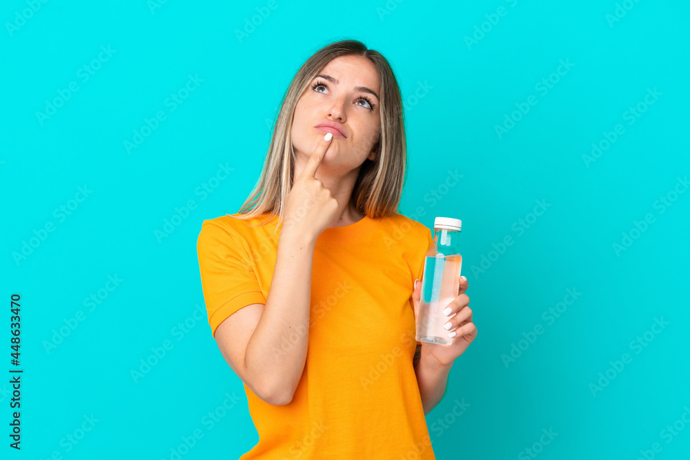 Young Romanian woman with a bottle of water isolated on blue background having doubts while looking up Young Romanian woman with a bottle of water isolated on blue background having doubts while looking up
