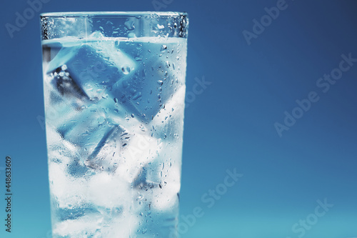 Glass with water and ice cubes on a blue background