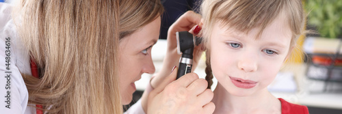 Doctor examines ear with an otoscope to little girl