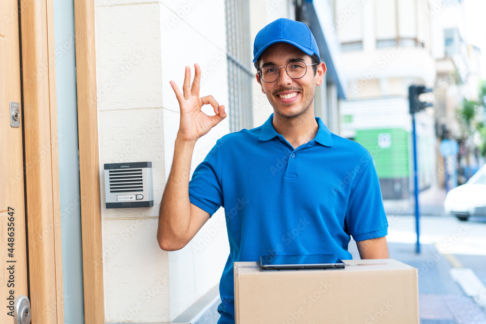 Young delivery man at outdoors holding boxes and a tablet and doing OK sign Young delivery man at outdoors holding boxes and a tablet and doing OK sign