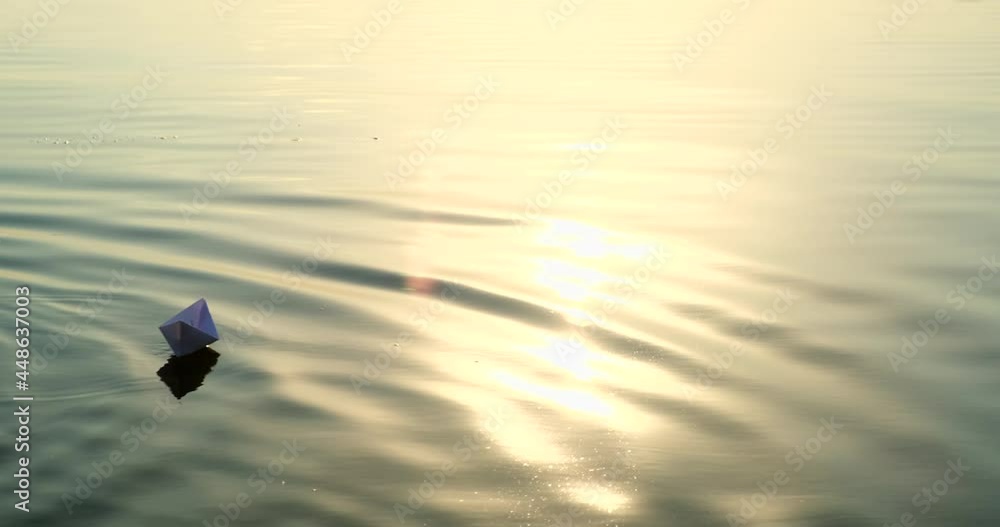 Ship made from paper swimming on water surface in evening or early morning. Homemade paper boats floating in the river with a beautiful sunset or sunrise background. Launching the ship into the water Ship made from paper swimming on water surface in evening or early morning. Homemade paper boats floating in the river with a beautiful sunset or sunrise background. Launching the ship into the water