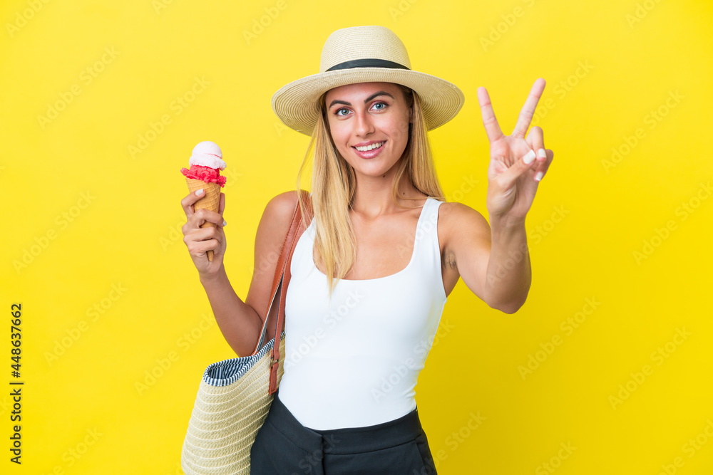 Blonde Uruguayan girl in summertime holding ice cream isolated on yellow background smiling and showing victory sign Blonde Uruguayan girl in summertime holding ice cream isolated on yellow background smiling and showing victory sign