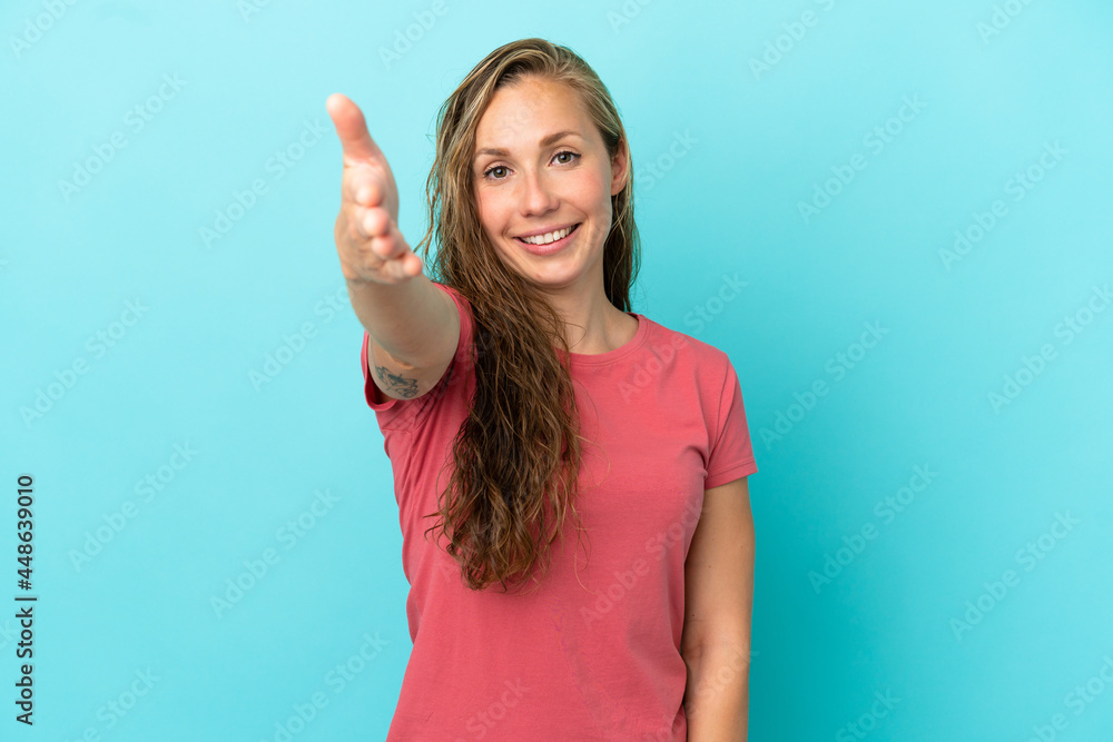 Fototapeta premium Young caucasian woman isolated on blue background shaking hands for closing a good deal