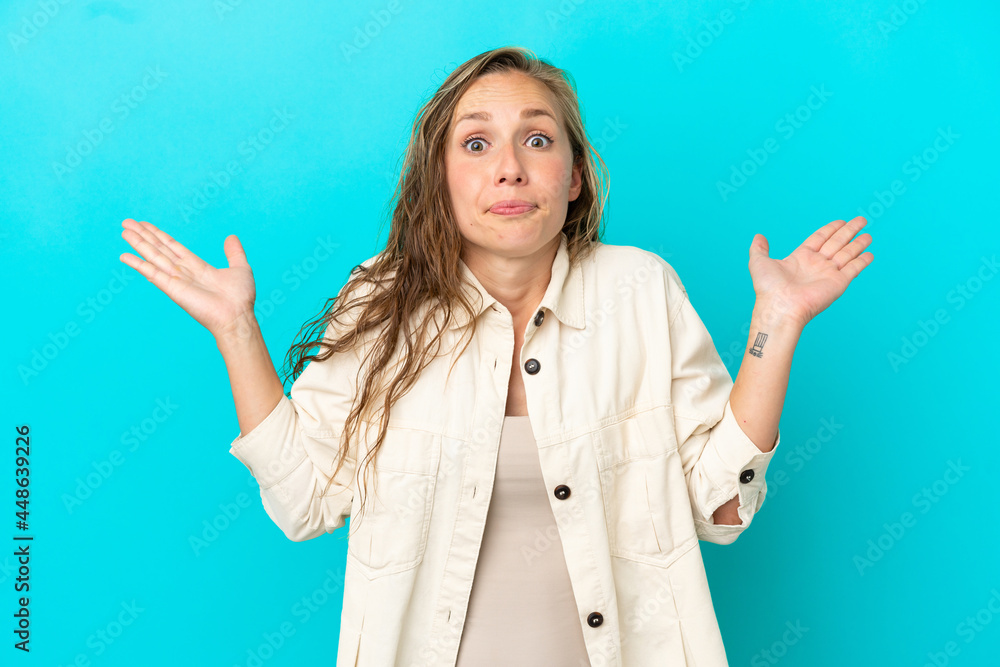 Young caucasian woman isolated on blue background making doubts gesture Young caucasian woman isolated on blue background making doubts gesture
