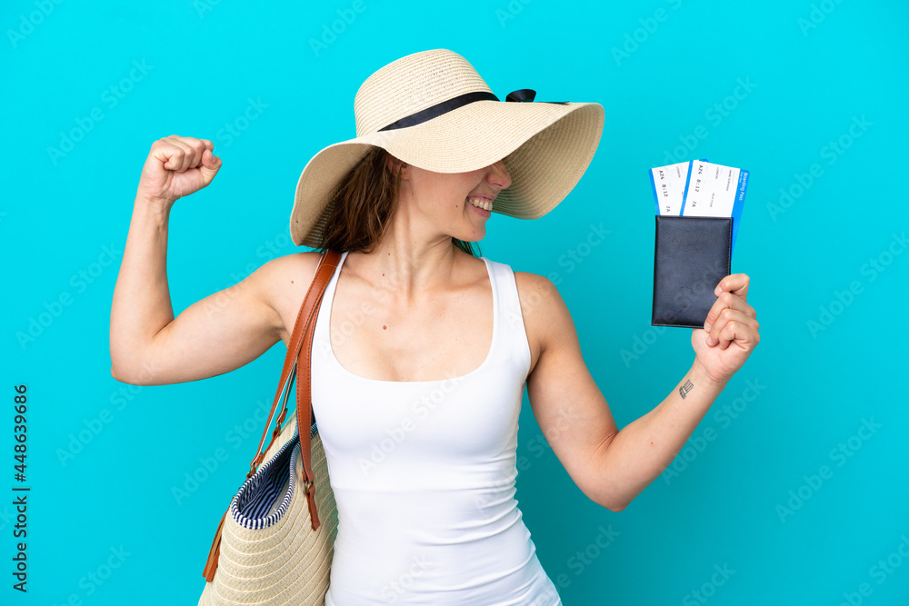 Young caucasian woman holding a beach bag and passport with pamel isolated on blue background celebrating a victory Young caucasian woman holding a beach bag and passport with pamel isolated on blue background celebrating a victory