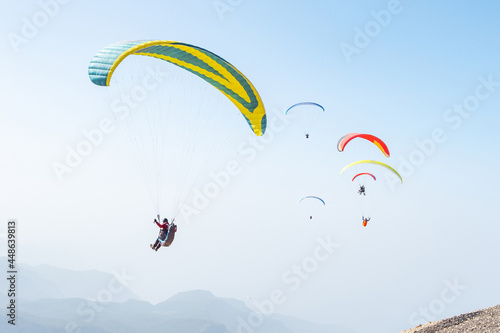 Paragliders take off from mountain top and fly in blue sky
