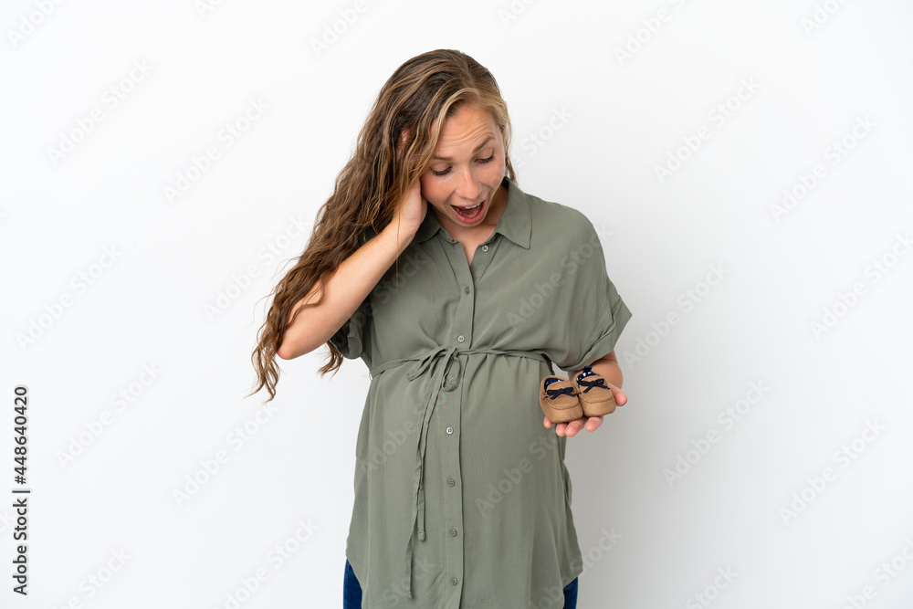Young caucasian woman isolated on white background pregnant and holding baby booties with surprised expression Young caucasian woman isolated on white background pregnant and holding baby booties with surprised expression