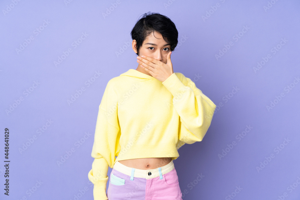 Young Vietnamese woman with short hair over isolated purple background covering mouth with hand Young Vietnamese woman with short hair over isolated purple background covering mouth with hand