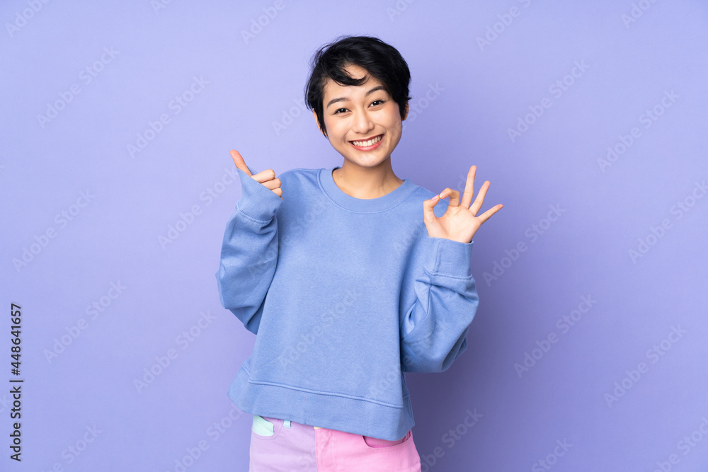 Young Vietnamese woman with short hair over isolated purple background showing ok sign and thumb up gesture Young Vietnamese woman with short hair over isolated purple background showing ok sign and thumb up gesture