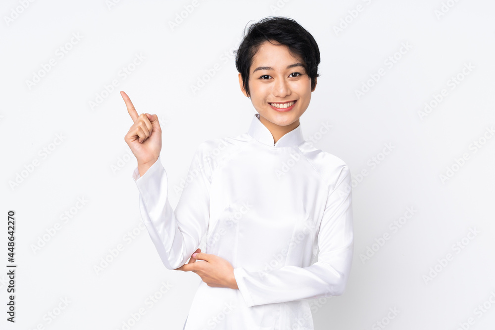 Young Vietnamese woman with short hair wearing a traditional dress over isolated white background happy and pointing up Young Vietnamese woman with short hair wearing a traditional dress over isolated white background happy and pointing up